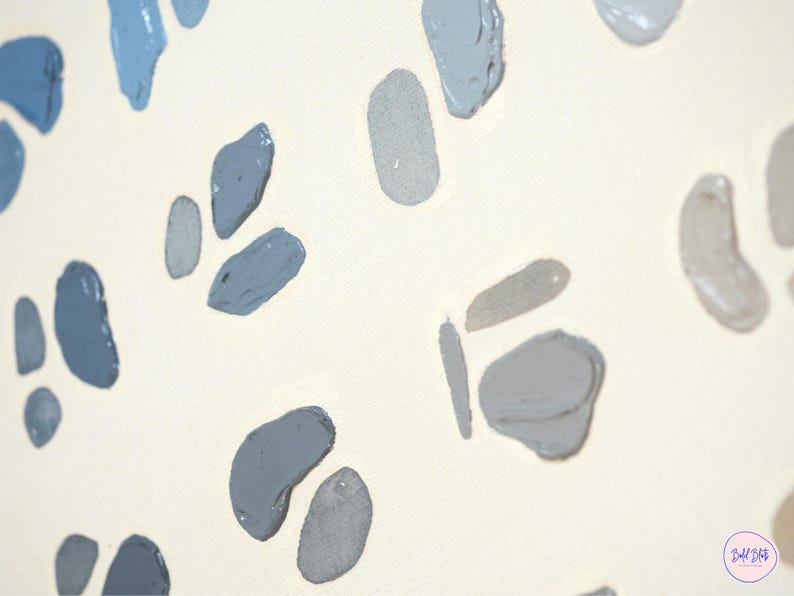 May include: Close-up of a canvas with a cream-colored background. The canvas is decorated with irregular, abstract shapes in shades of blue and gray. The shapes are painted with visible brushstrokes, creating a textured effect.