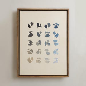 May include: Abstract art print featuring a series of organic shapes in shades of blue, gray, and beige, arranged in a grid pattern. The artwork is framed in a natural wood frame, creating a modern and minimalist aesthetic.
