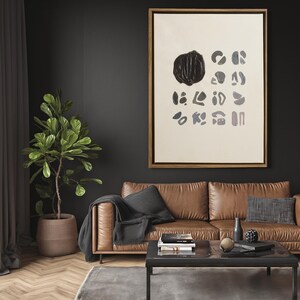 May include: A brown leather sofa with a black throw blanket and a black and white abstract painting hanging on the wall above it. The sofa is in a living room with a coffee table and a potted plant.