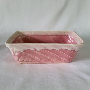 Könnte beinhalten: Ein rosafarbener Keramik-Pflanztopf mit weißem Überzug und einem Spiralmuster. Der Topf ist rechteckig und hat einen leicht abgerundeten Boden.
