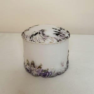 May include: White ceramic jar with a floral design in shades of purple and black. The jar has a round shape and a lid.