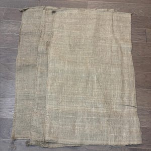 May include: Several beige burlap sacks are stacked on a wooden surface. The sacks are made of a coarse, woven material, and appear to be empty. The sacks are rectangular in shape and have a simple, utilitarian design.