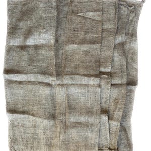 May include: A folded, beige burlap sack with a rough, woven texture. The sack is made of natural fibers and has a rustic, vintage look.
