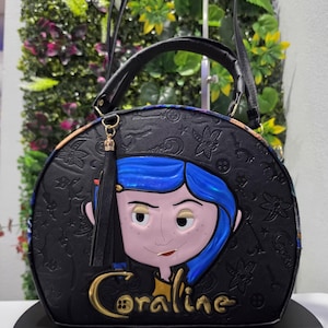 May include: A black dome-shaped handbag featuring an embossed pattern of keys and buttons. The front displays a raised, colorful character graphic of Coraline with blue hair and the name Coraline in gold lettering. It includes a black tassel charm.
