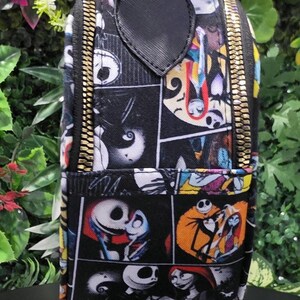 May include: A rectangular mini backpack featuring a comic book style print of Jack Skellington and Sally from The Nightmare Before Christmas. The bag has a black top handle, gold-toned metal zippers, and a black strap with a gold-toned metal clasp.