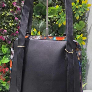 Puede incluir: Una mochila negra con acabado texturizado, que cuenta con dos correas ajustables para los hombros con hebillas y anillos de metal dorado. Los laterales de la bolsa muestran un patr&oacute;n colorido de mariposas y elementos florales.