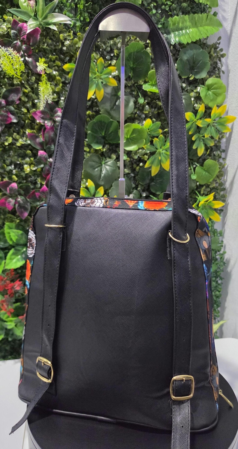 Puede incluir: Una mochila negra con acabado texturizado, que cuenta con dos correas ajustables para los hombros con hebillas y anillos de metal dorado. Los laterales de la bolsa muestran un patr&oacute;n colorido de mariposas y elementos florales.