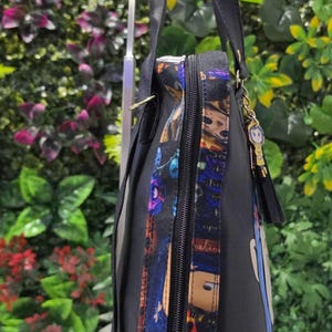 Puede incluir: Una mochila negra que presenta un panel lateral con un estampado de personajes coloridos, un cierre de cremallera negro y un peque&ntilde;o dije colgante unido al asa superior. La bolsa tiene correas negras ajustables y un dise&ntilde;o vertical.
