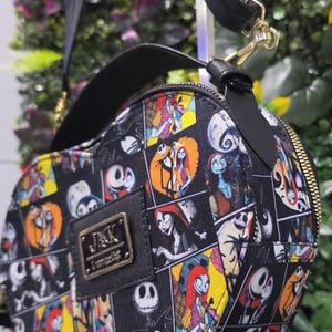 May include: A heart-shaped crossbody bag featuring a black and white grid pattern with colorful illustrations of Jack Skellington and Sally from The Nightmare Before Christmas. The bag has a black top handle, a shoulder strap, and a gold-tone metal plaque.