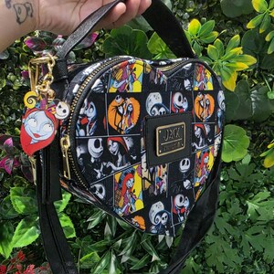 May include: A heart-shaped crossbody bag featuring a black, yellow, and white comic-style print of Jack Skellington and Sally. The bag includes a black top handle, a gold-tone zipper, and a metal plaque with the text JACK LOUNGEFLY.