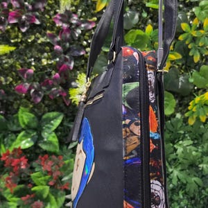 Puede incluir: Un bolso tote negro con dos correas para el hombro y un panel lateral con un estampado gr&aacute;fico colorido. La parte frontal del bolso muestra una ilustraci&oacute;n de personaje estilizada con cabello azul y letras doradas. Cierre de cremallera lateral.