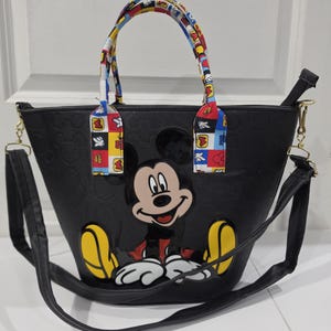 Pu&ograve; includere: Una borsa tote nera con un motivo di Topolino in rilievo all'esterno e una grande grafica colorata di Topolino sul davanti. La borsa include due manici superiori con un motivo multicolore e una tracolla nera rimovibile.
