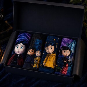 May include: A dark blue box set containing four pairs of socks with character illustrations. The socks feature images of a girl in a yellow raincoat, a girl in a red coat, and other characters. A black cat figurine and a lantern are in the background.