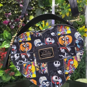 May include: A heart-shaped crossbody bag featuring a black background with a colorful comic-style print of Jack Skellington and Sally from The Nightmare Before Christmas. The bag includes a black top handle, a shoulder strap, and a gold metal plaque with the text JACK Loungefly.