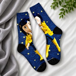 May include: A pair of crew socks featuring a cartoon character in a yellow coat and blue pants, set against a dark blue background with a swirling pattern and yellow stars. The socks have black heels and toes.