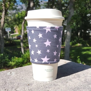 May include: A gray and pink reusable coffee cup sleeve with a star pattern. The text "Reusable, Recyclable, Re-enjoyable" is printed on the sleeve.