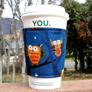 Könnte beinhalten: Ein weißer To-Go-Kaffeebecher mit einer blauen und braunen Eulen-Stoffhülle. Auf dem Becher steht "YOU.". Die Hülle trägt den Text "Find out what else you can do at starbucks.com/sharedplanet."
