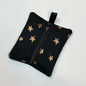 Può includere: Piccola pochette nera con motivo a stelle dorate. Presenta una chiusura a zip nera e un piccolo passante in tessuto nero. La pochette rettangolare è probabilmente realizzata in un materiale morbido. Misura circa 10 cm di lunghezza.