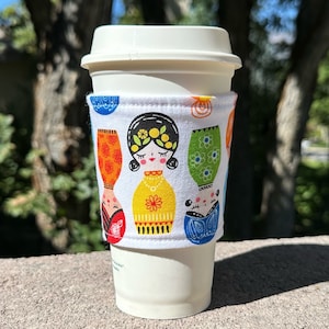 Varm eller isig tygkaffemugg / mugghylsa / kaffehylsa -- Matrjosjka inbäddad ryska stapeldockor på vitt -- platt frakt
