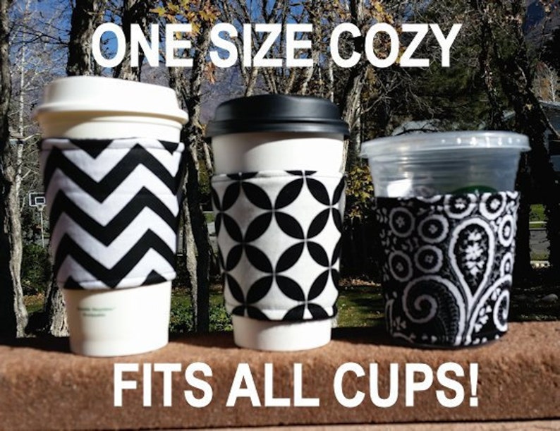 May include: Three different black and white patterned cup cozies. The cozies are made of fabric and fit all sizes of cups. The text "ONE SIZE COZY" is at the top of the image and the text "FITS ALL CUPS!" is at the bottom of the image.