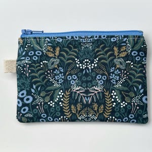 May include: A small zippered pouch with a dark blue background and a floral pattern in shades of blue, white, and gold. The zipper is light blue.