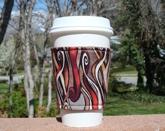 May include: A white coffee cup with a colourful fabric sleeve. The sleeve has a swirling pattern of red, brown, and white.