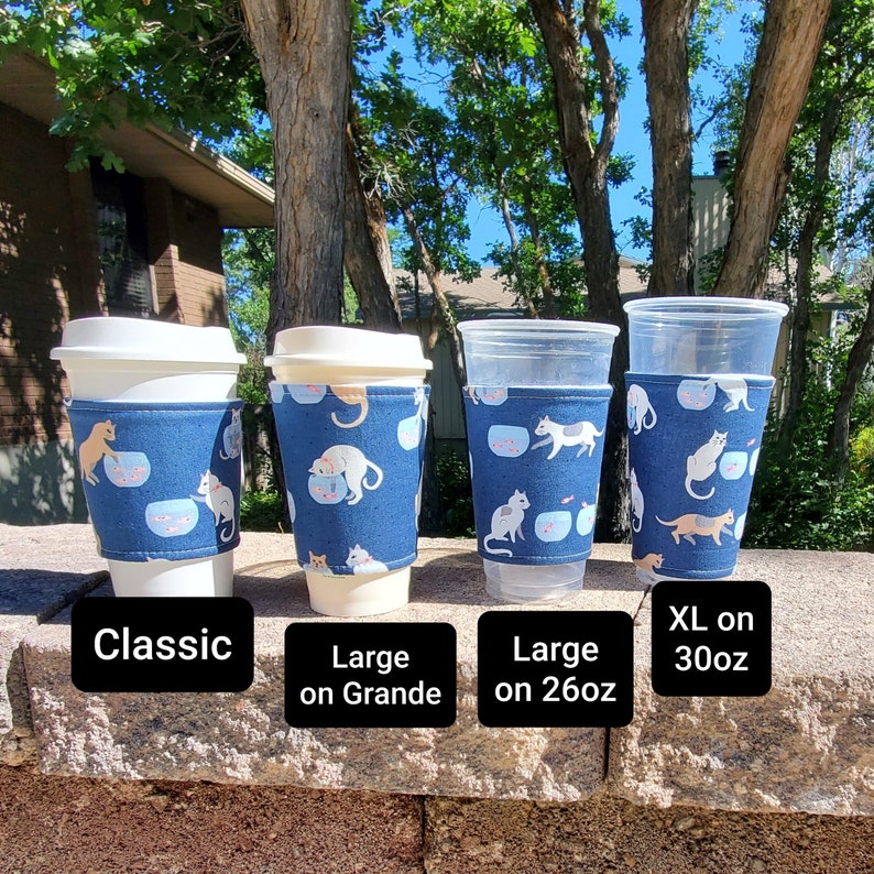 May include: Four coffee cup sleeves with a blue background and a white cat pattern. The sleeves are shown on different sized cups, labeled "Classic", "Large on Grande", "Large on 26oz", and "XL on 30oz".