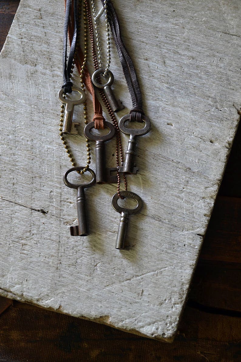 May include: A set of six antique keys on leather cords and chains. The keys are silver and have a worn, rustic look. The cords are brown and black.