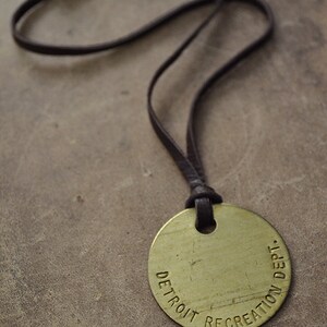 May include: A brown leather cord necklace with a round brass pendant that reads "DETROIT RECREATION DEPT."