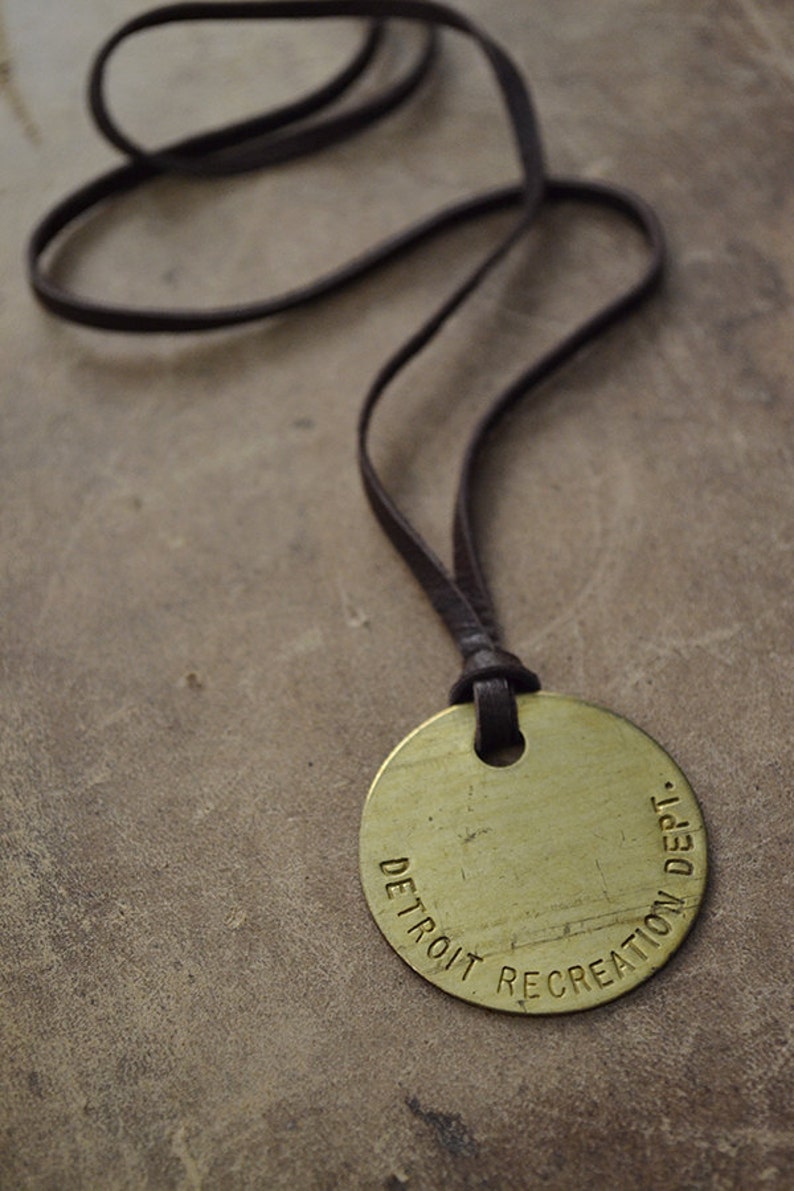 May include: A brown leather cord necklace with a round brass pendant that reads "DETROIT RECREATION DEPT."