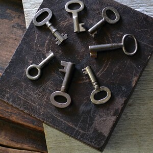 May include: A collection of seven antique keys arranged in a starburst pattern on a dark brown surface. The keys are made of metal and have a worn, aged appearance.