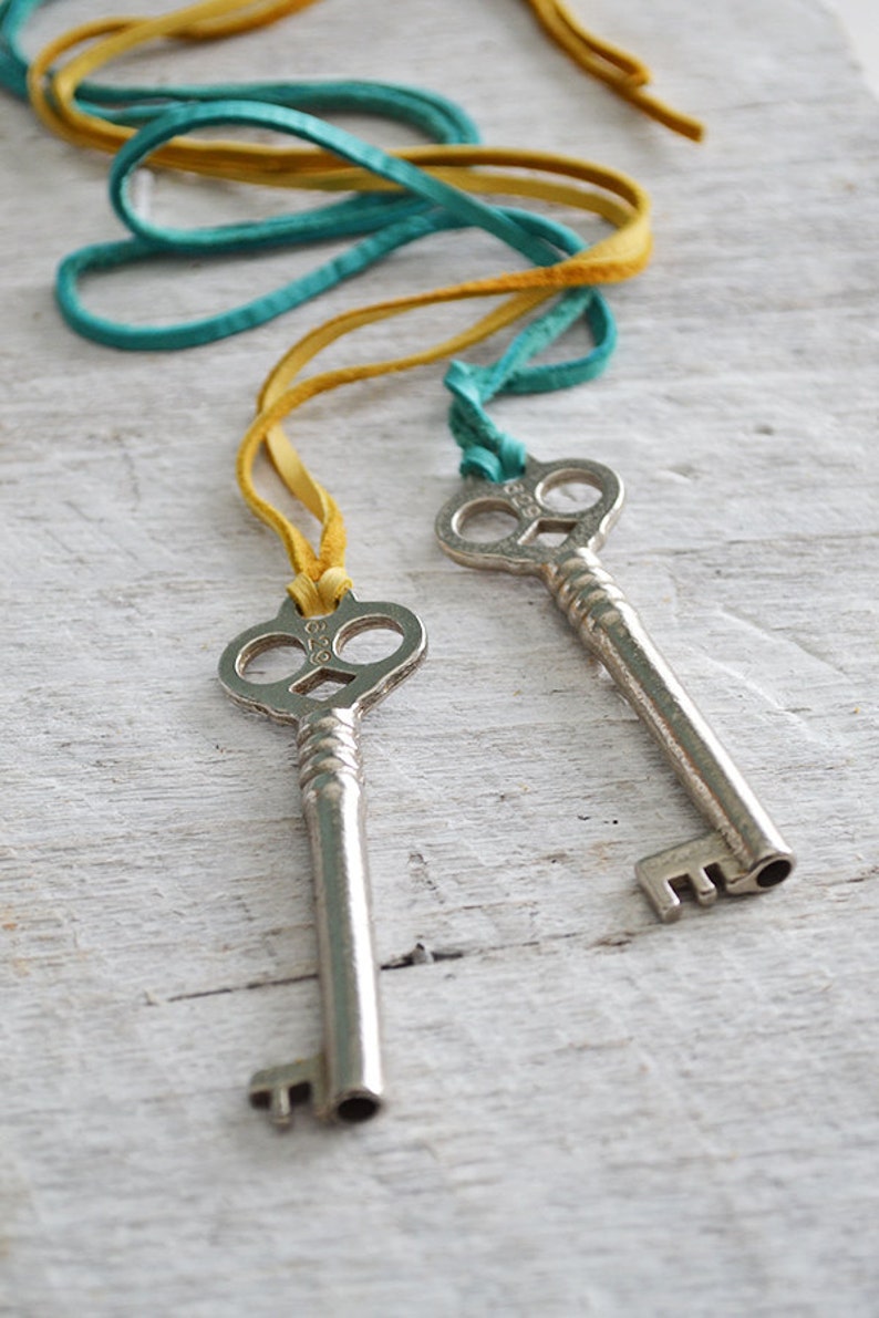 Op de afbeelding: Twee antieke zilveren sleutels met sierlijke ontwerpen, hangend aan een geel en turquoise leren koord.
