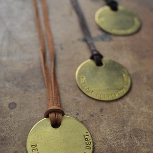 May include: Three brass pendants with leather cords. Each pendant has the text "DETROIT RECREATION DEPT." engraved around the edge.