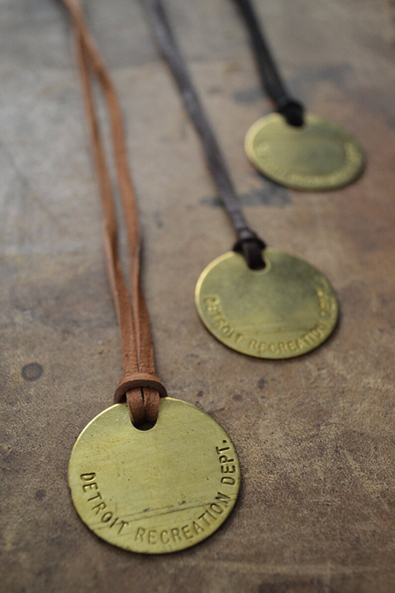 May include: Three brass pendants with leather cords. Each pendant has the text "DETROIT RECREATION DEPT." engraved around the edge.