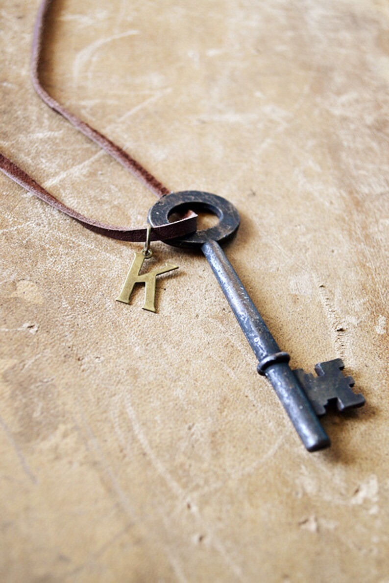 May include: A brown leather cord necklace with a large antique-style key pendant and a gold letter 'K' charm.