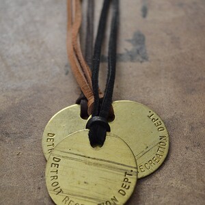 May include: Two round brass tags with black leather cord. The tags are engraved with "DETROIT RECREATION DEPT."