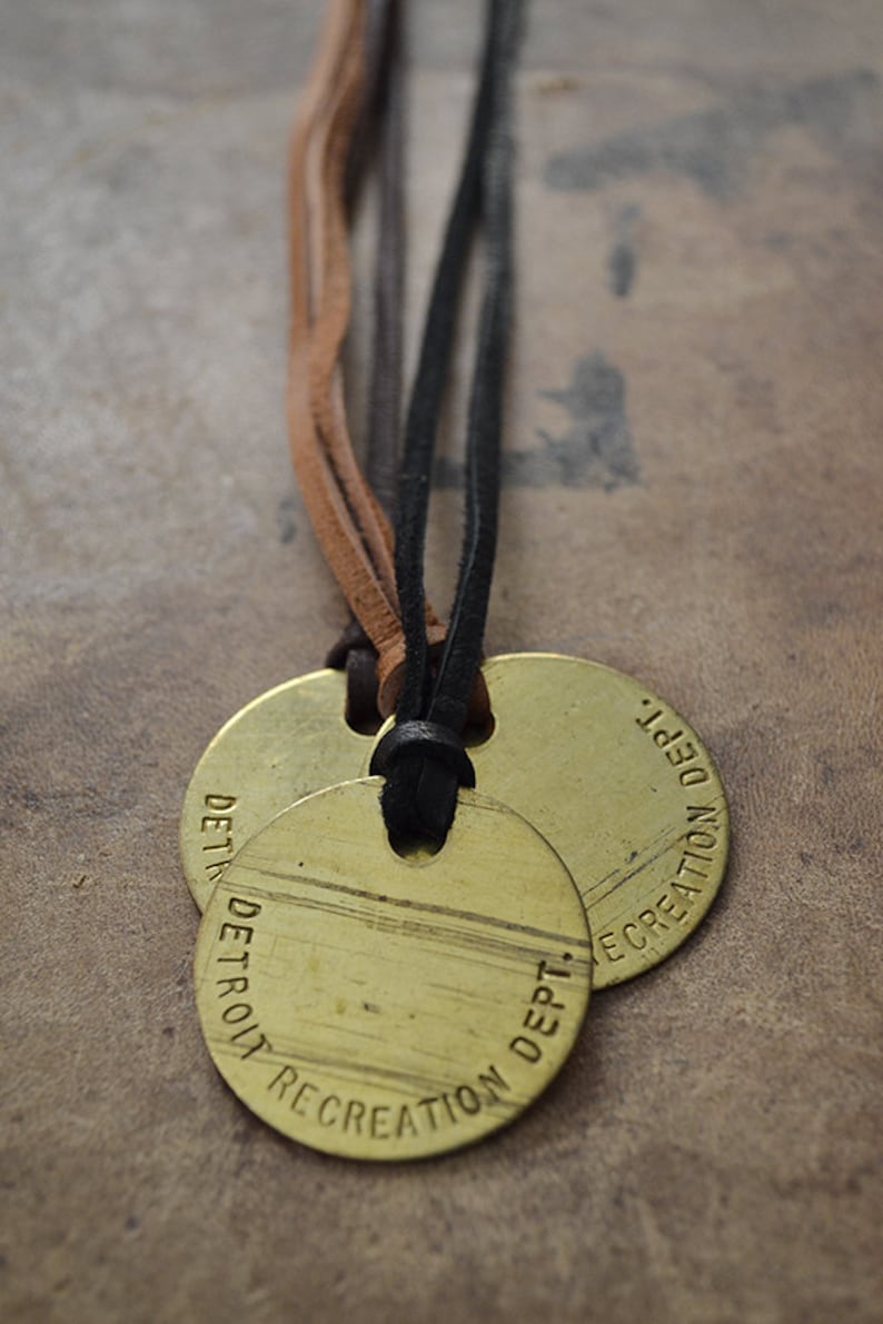 May include: Two round brass tags with black leather cord. The tags are engraved with "DETROIT RECREATION DEPT."