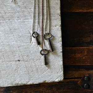 May include: Three antique keys on chains, hanging from a white surface. The keys are silver, gold, and copper.