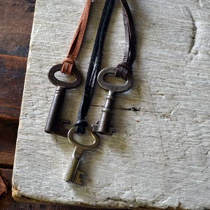 May include: Three antique keys on leather cords. The keys are silver with a tarnished finish. The cords are brown, black, and brown.