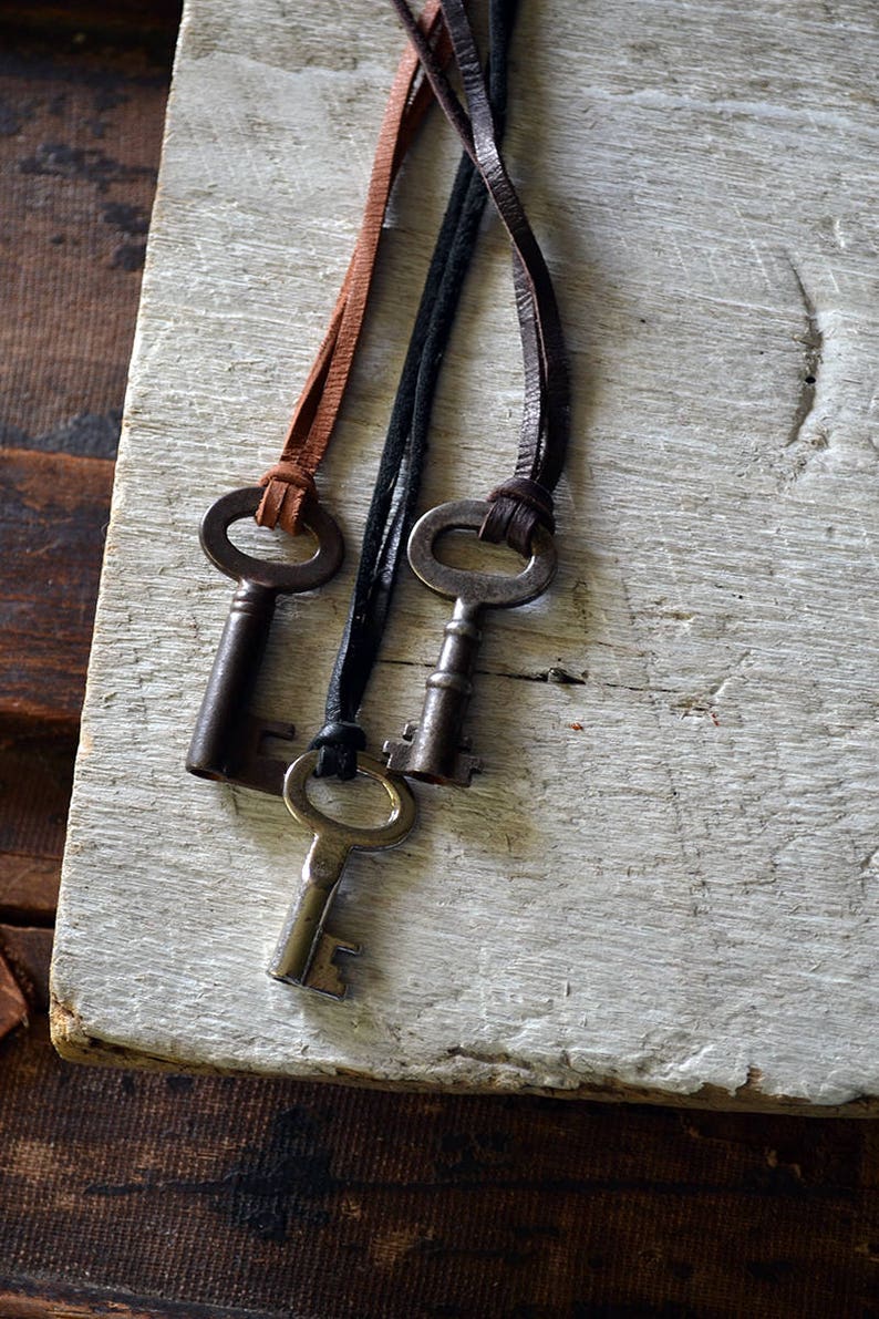 May include: Three antique keys on leather cords. The keys are silver with a tarnished finish. The cords are brown, black, and brown.