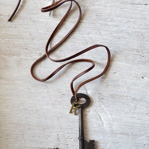 May include: A brown leather cord necklace with an antique skeleton key pendant and two gold letter charms.