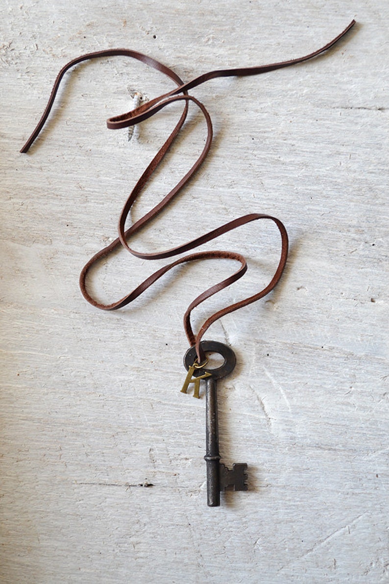 May include: A brown leather cord necklace with an antique skeleton key pendant and two gold letter charms.
