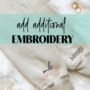 May include: A beige sweatshirt with the text "add additional EMBROIDERY" at the top. The sweatshirt has two embroidered designs: "msb" with a heart and "mlb" with two hearts. The date "3-17-2023" is embroidered on the right sleeve.