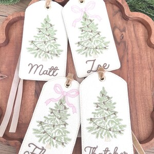 Pu&ograve; includere: Quattro etichette regalo di Natale bianche con alberi di Natale verdi ricamati e nomi: Matt, Joe, Flora e Thatcher. Due etichette hanno fiocchi rosa. Ogni etichetta ha un occhiello dorato e un nastro beige.