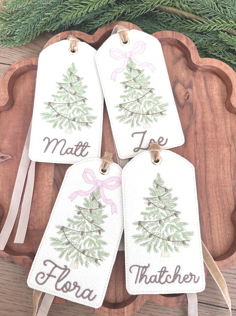 Pu&ograve; includere: Quattro etichette regalo di Natale bianche con alberi di Natale verdi ricamati e nomi: Matt, Joe, Flora e Thatcher. Due etichette hanno fiocchi rosa. Ogni etichetta ha un occhiello dorato e un nastro beige.