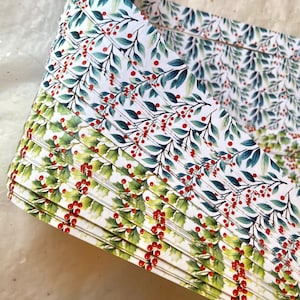 May include: A stack of white paper with a green and red holly berry pattern. The paper is folded in half and the edges are visible.