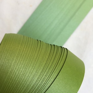 May include: A roll of green paper with a satin finish. The paper is rolled up tightly and the edges are visible.