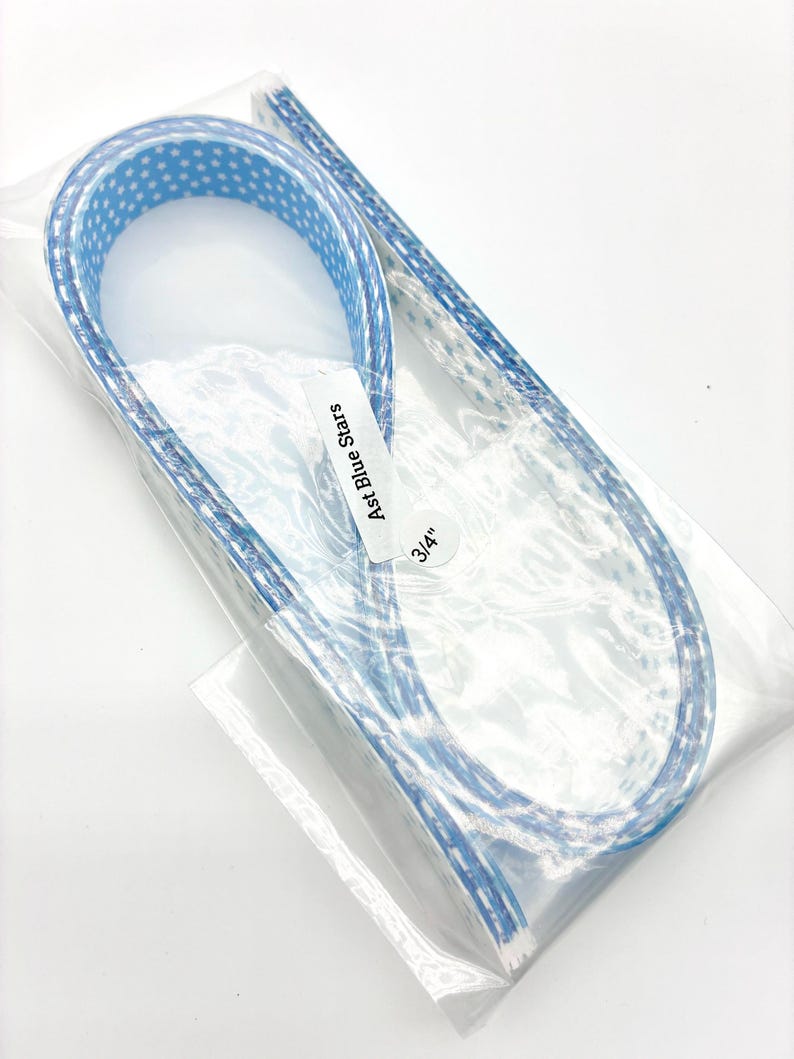 May include: A package containing a blue ribbon with white star patterns. The ribbon is labeled "Ast Blue Stars" and is 3/4" wide. The ribbon is in a clear plastic package.