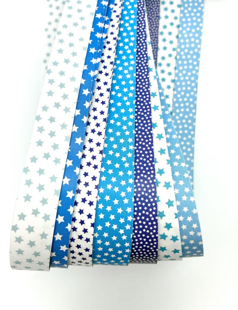 May include: A collection of blue and white patterned paper strips. The patterns include stars and dots in various shades of blue, from light to dark. The strips are arranged in a fan shape, showcasing the different designs.
