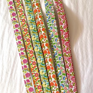 May include: Eight strips of paper with a floral pattern in shades of red, green, blue, and yellow. The strips are arranged vertically and are all the same length.